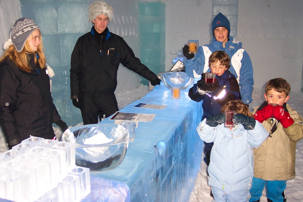 Photo of my wife with our three children standing in front of the ice bar where two servers are standing. Everyone is holding glasses made of ice filled with juice.