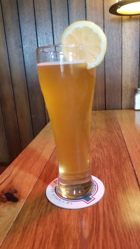 A tall glass filled with Hefeweizen beer. The glass has unfortunately a slice of lemon on top.