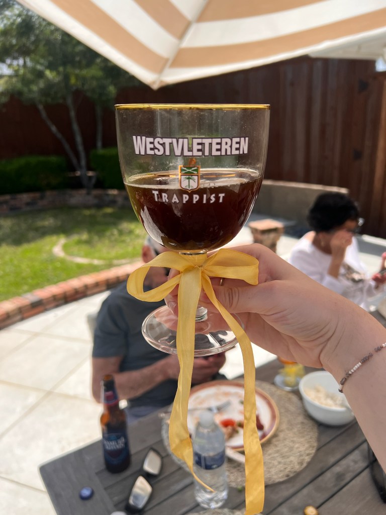 My daughter holding a Westvleteren 12 glass with a bow. Grandpa and grandma sitting on chairs in the background.