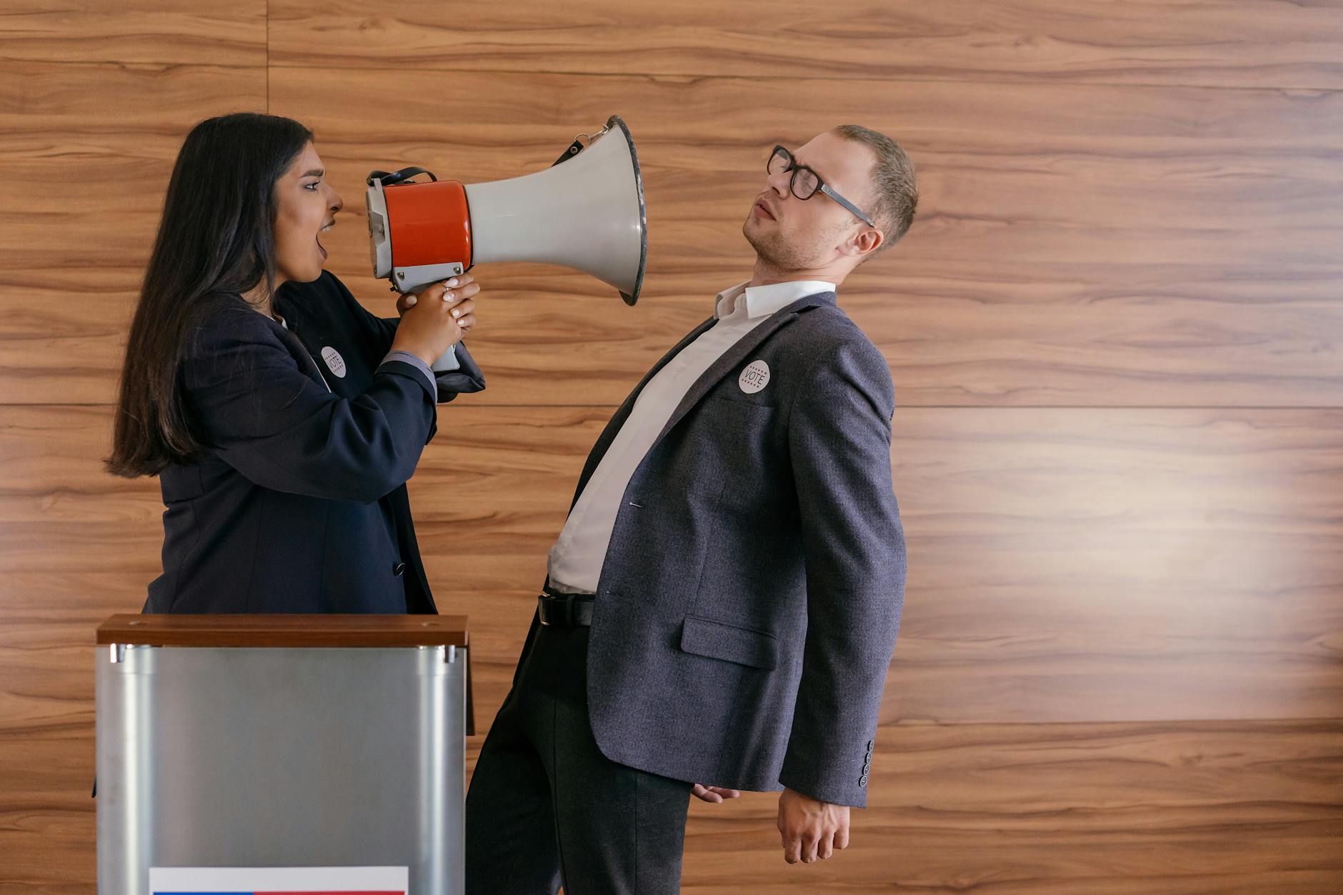 A woman is shouting into the man's face using a megaphone.