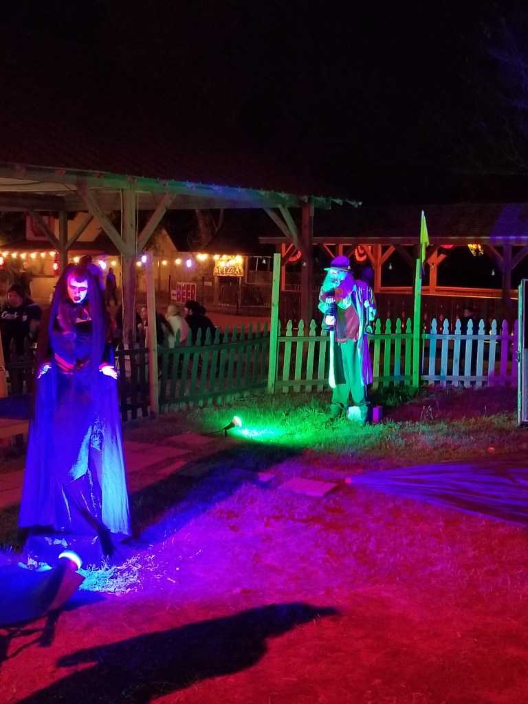 The photos show two spooky props lit up by colorful lights. They are standing in the corner of the playground.