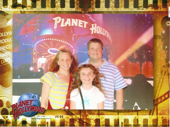 The picture shows a woman (mother) and a man (father) and their daughter. Planet Hollywood is in the background.