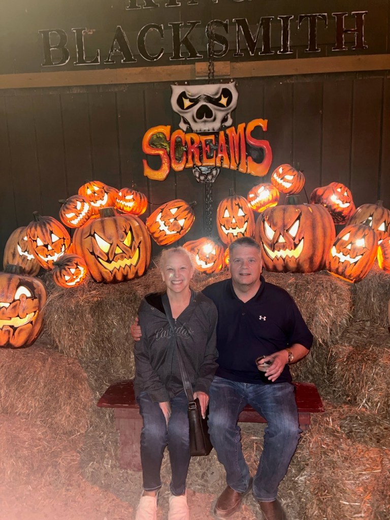 Claudia dressed in black and blue jeans on my right. I am wearing dark blue and blue jeans. We are sitting in front of dozens of Jack’O Lanterns