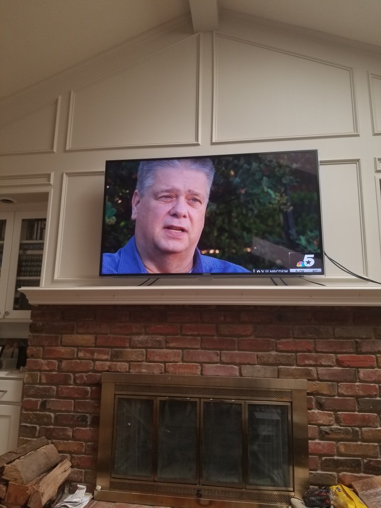 A photo of my TV above the fireplace. I am on the TV screen.
