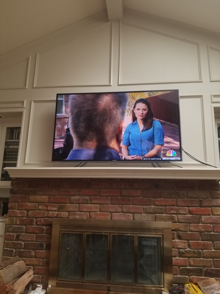 A photo of my TV above the fireplace. I am on the TV screen.