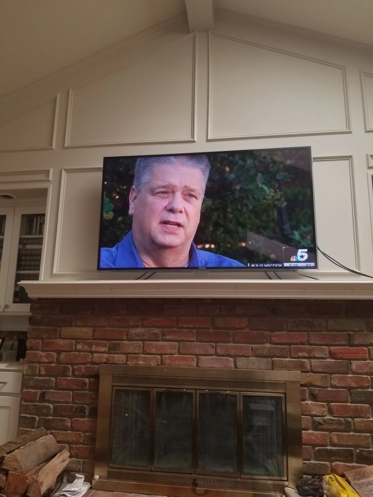 A photo of my TV above the fireplace. I am on the TV screen.