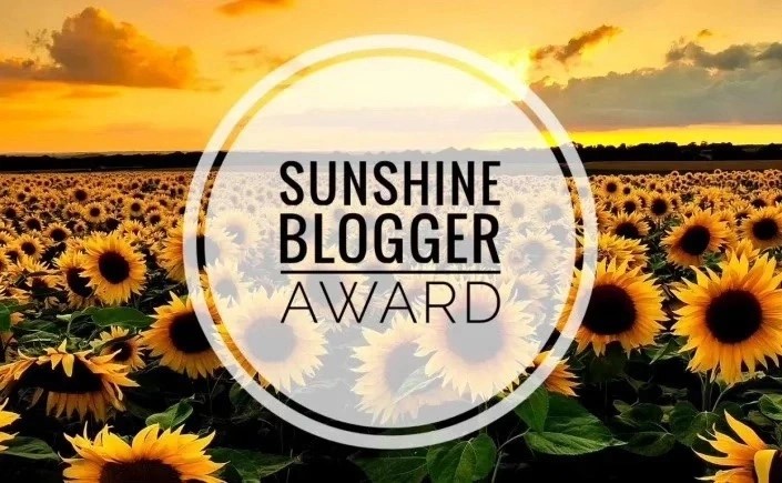 The picture says Sunshine Blogger Award, and, in the background, there are a lot of sun flowers.