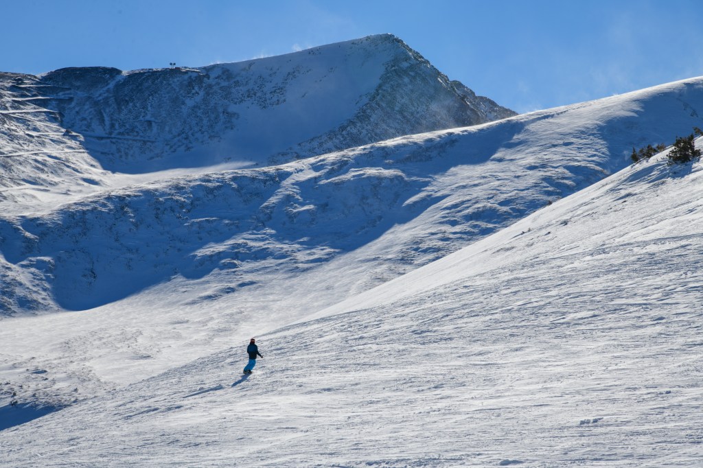 Summit view from Peak 8 at Breckenridge Ski Resort, Colorado. Snowboarder riding down in the mountains.