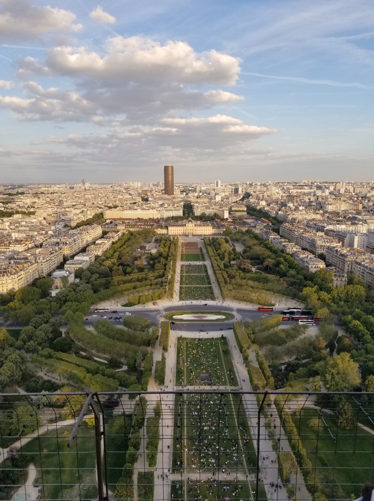 The view features a huge green garden and beautiful buildings. Champ de Mars is located next to the Eiffel Tower.
