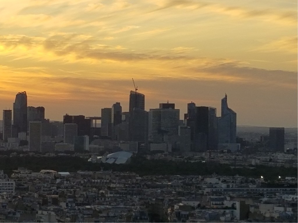 The skyscrapers in the distance are part of La Défense de Paris. The sun is setting, making it a beautiful photo.