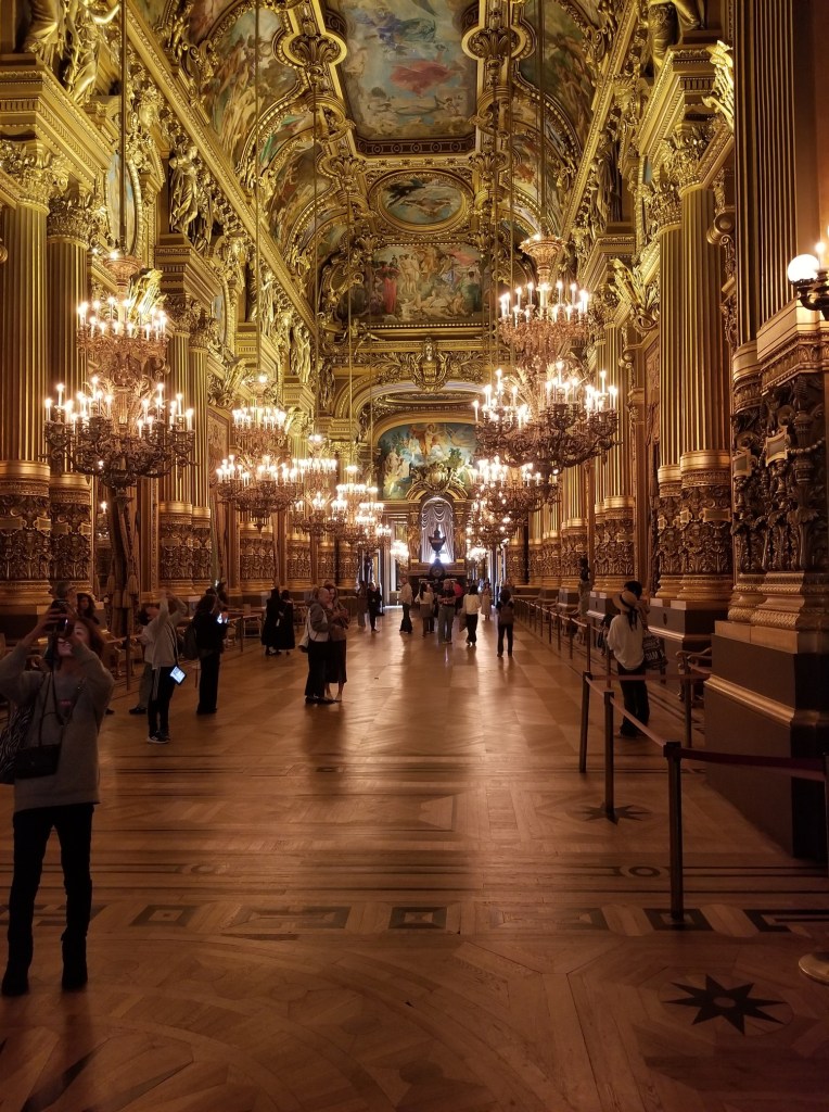 A very long and large hallway with dozens of chandeliers, golden columns, and enormous paintings. The most beautiful room in Palais Opéra Garnier.