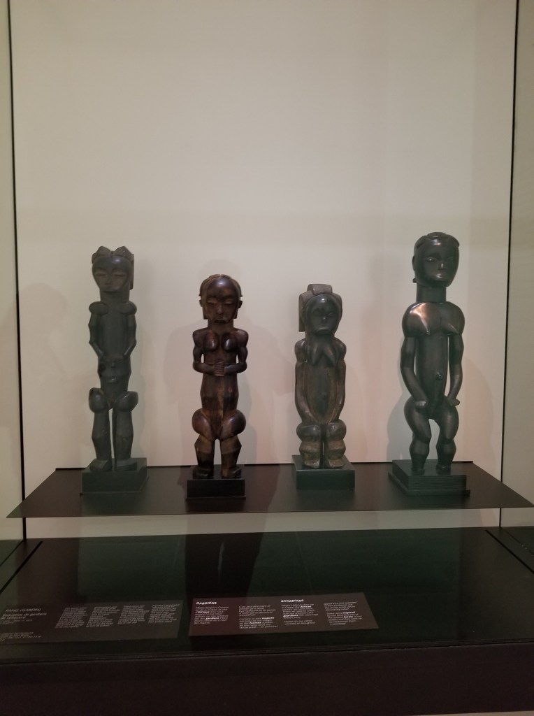 The photo shows four ancient wooden statues on display in the Musée de l'Orangerie.