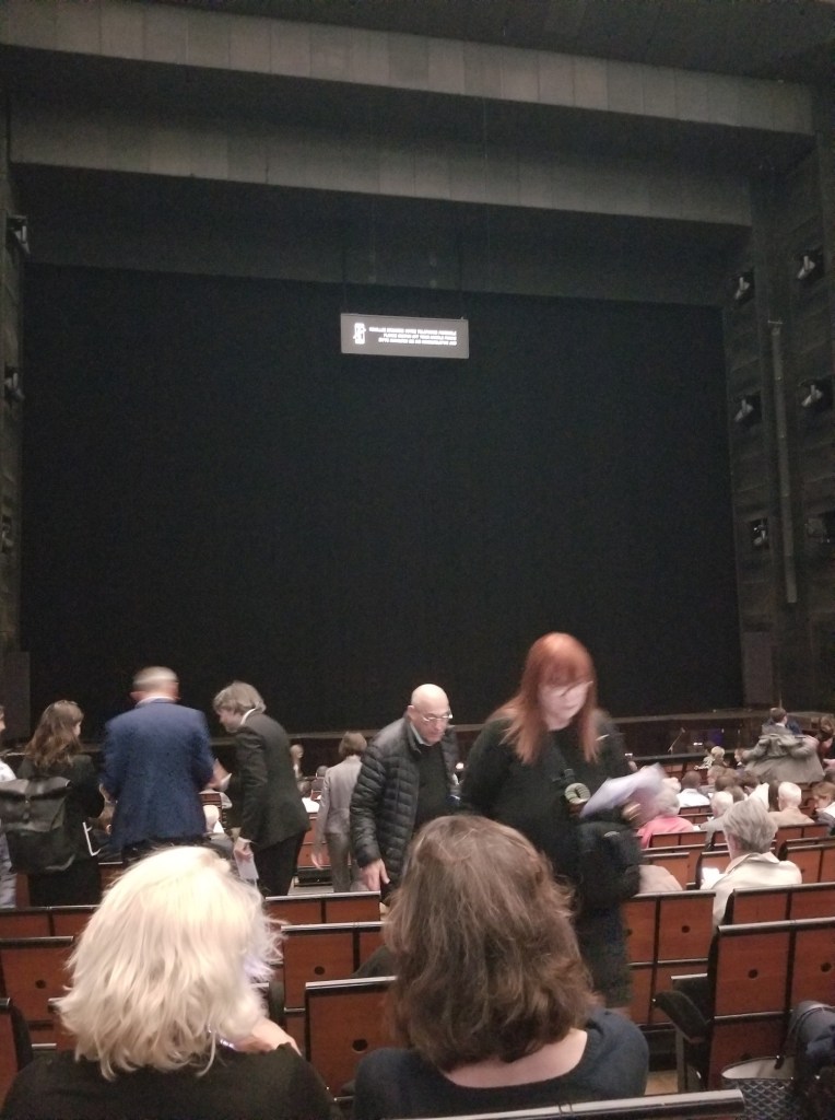 Photo of the scene at Opera at Opera National, Paris, France. There are a few people in the isles and in the seats. 