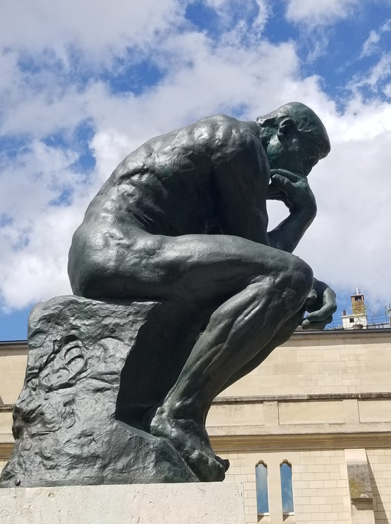 The statue is of a naked man sitting and thinking.