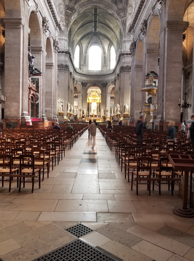 The inside of Saint Sulpice is large, with white columns and a tall, rounded ceiling.