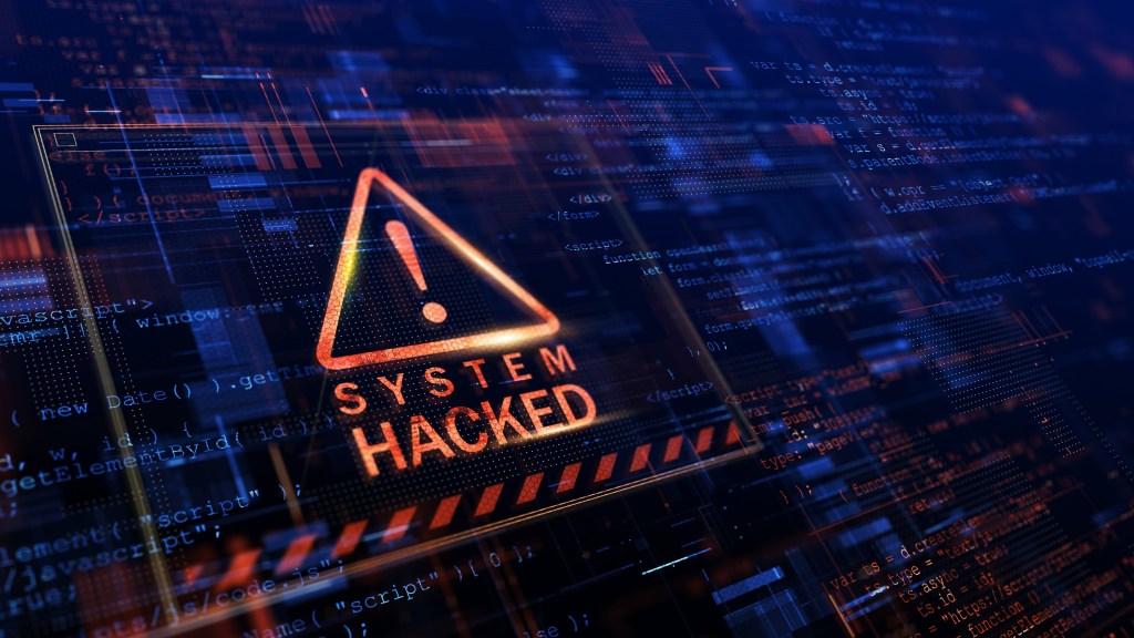 A picture of giant computer screen with a red warning triangle containing an exclamation mark. Underneath the triangle is the text “System Hacked”