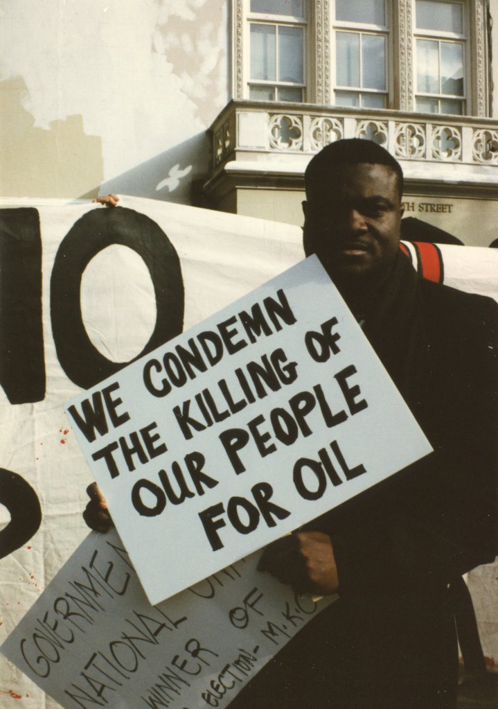 A black African holding a sign that says, “We condemn the killing of our people for oil.”