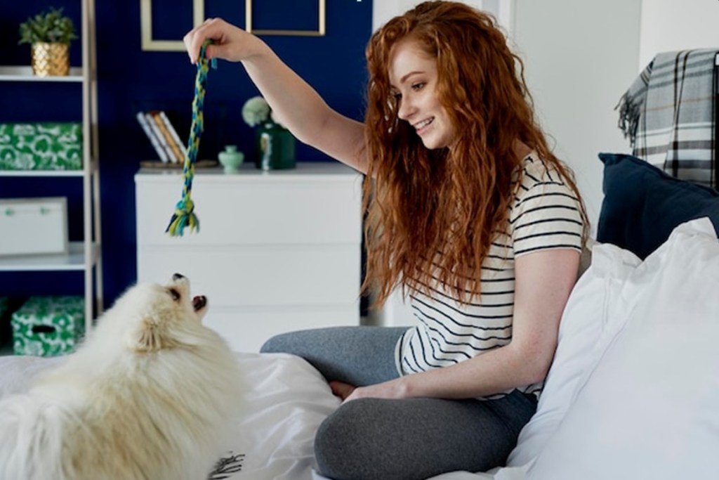 A red haired woman is playing with a small white fluffy dog.