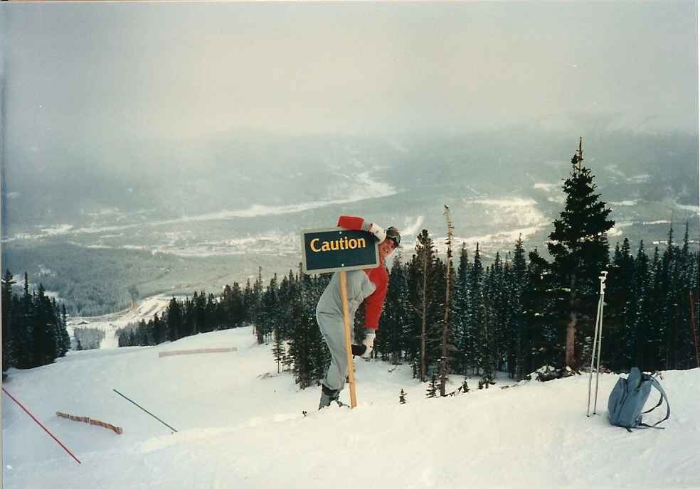 Me standing in the ski slope in Breckenridge leaning on a sign that says “Caution”