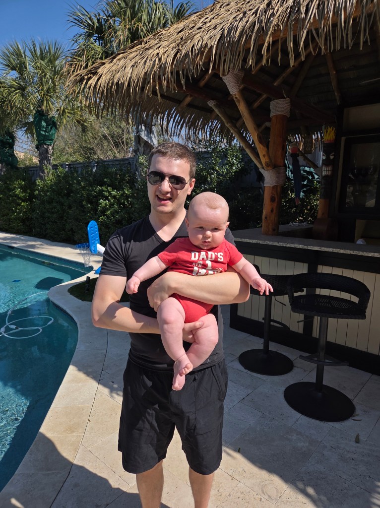 Our son standing by a pool and holding baby Jack.