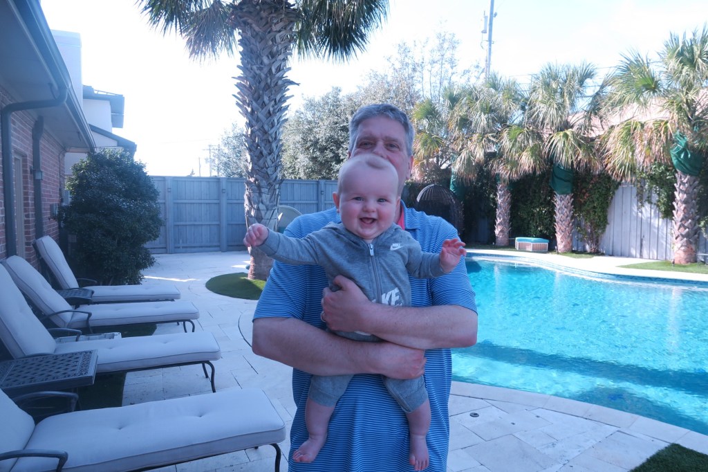 I am standing in front of a pool holding a happy baby Jack.