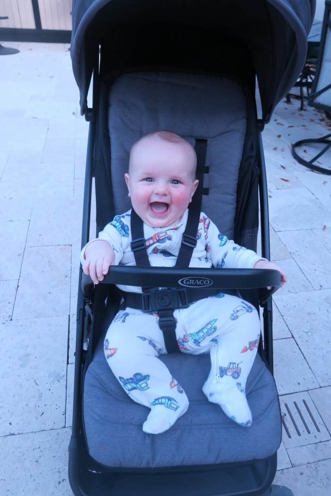 Baby Jack is sitting in a black stroller. He is laughing.