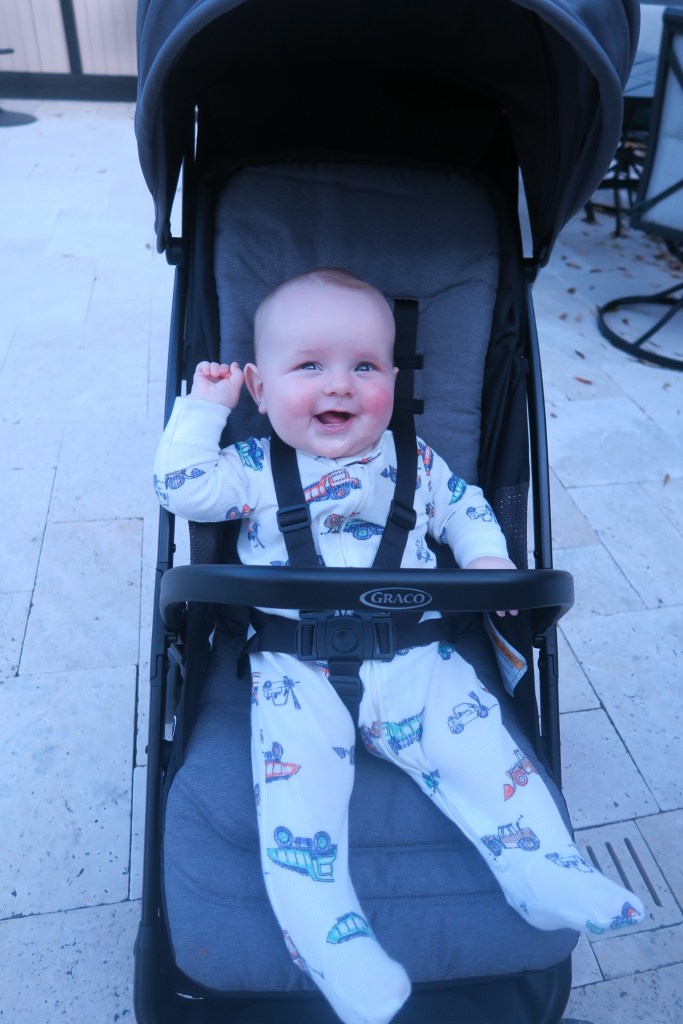 Baby Jack is sitting in a black stroller. He is laughing.