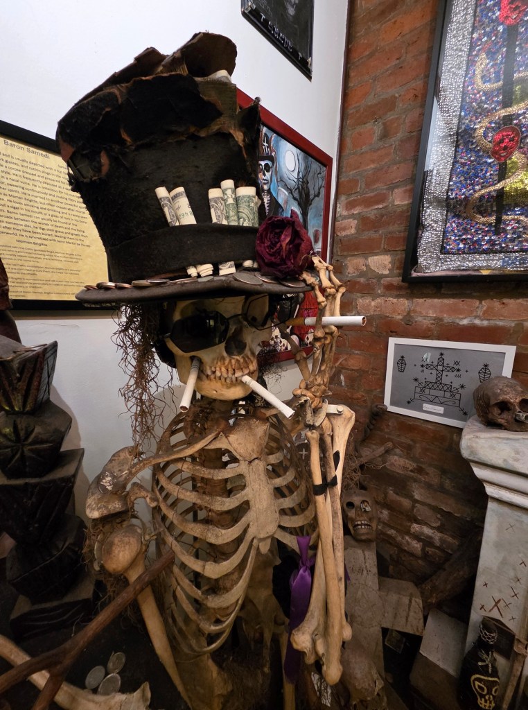 A skeleton wearing a black top hat. The skeleton has several cigarettes in its mouth.