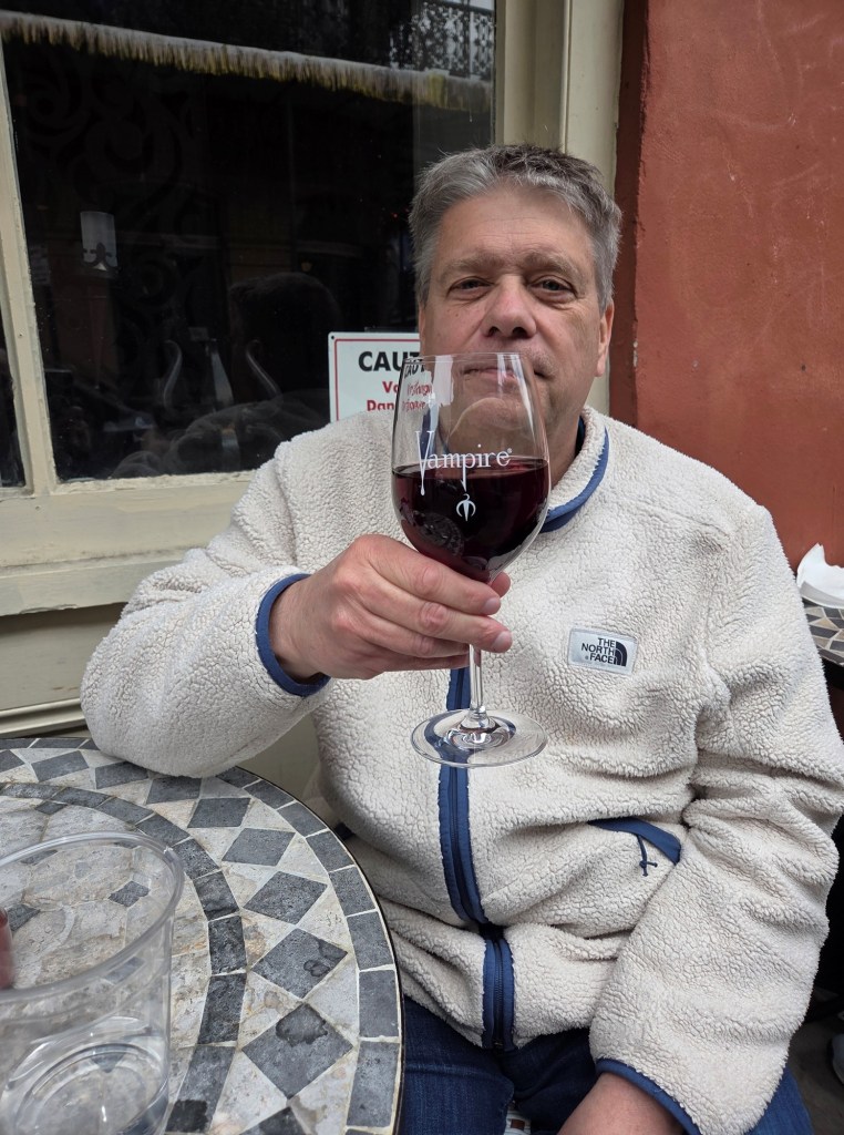 I am sitting on a chair in front of the Vampire Café drinking a glass of wine (Pinot Noir). The glass says Vampire Café.