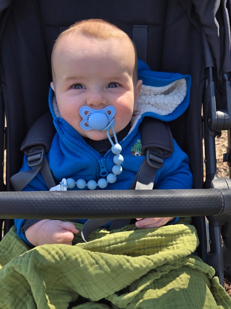 Baby in a stroller with a blue binky and wearing a blue coat.