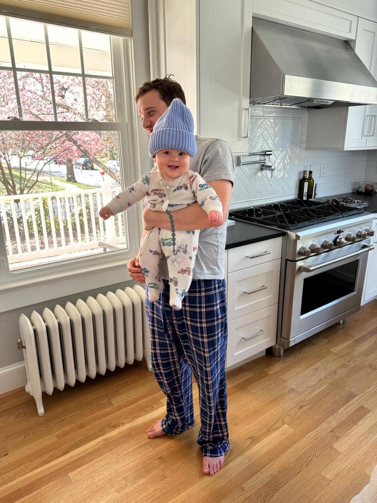 The photo shows my son holding a happy and laughing baby wearing a blue hat.