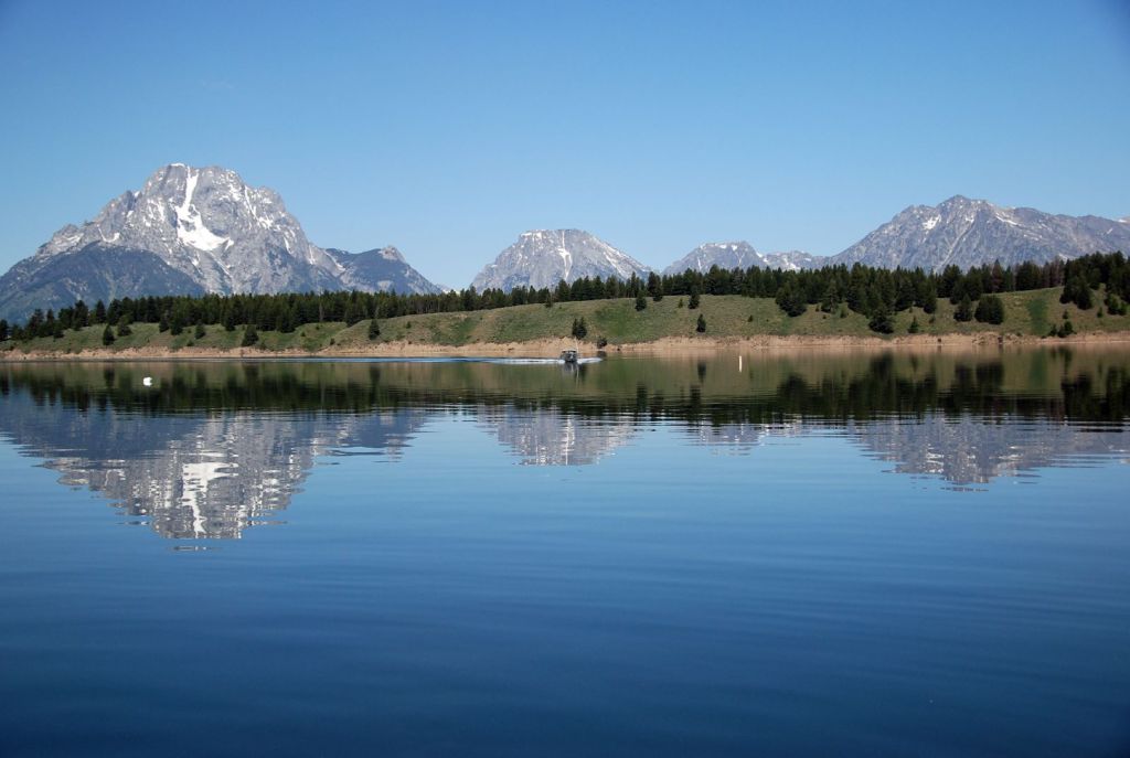 The Teton range towering an island is reflected in a lake.