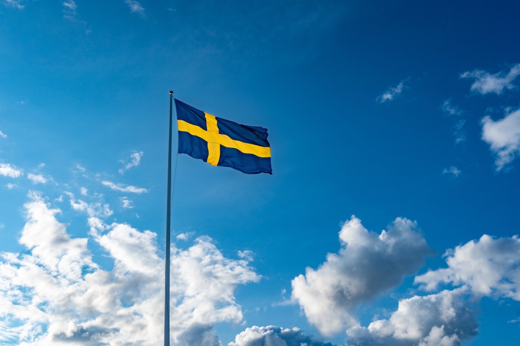 Swedish flag on blue sky with white clouds. 6 June. Flag. Celebration Holiday National Day Festive.