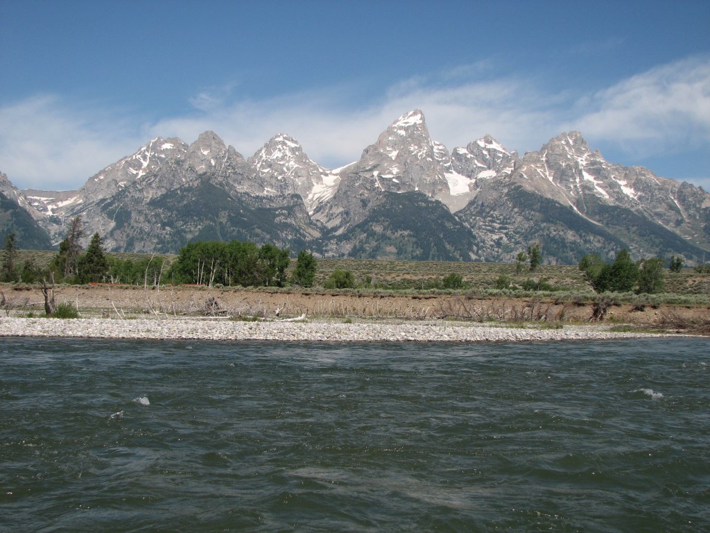Photo including a somewhat turbulent Snake River with the Teton mountain range in the background.