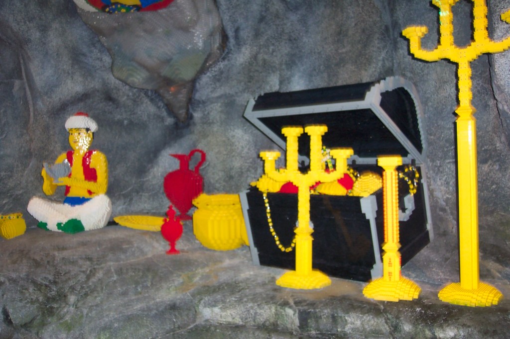 Aladdin is sitting surrounded by treasures including a large open treasure chest.