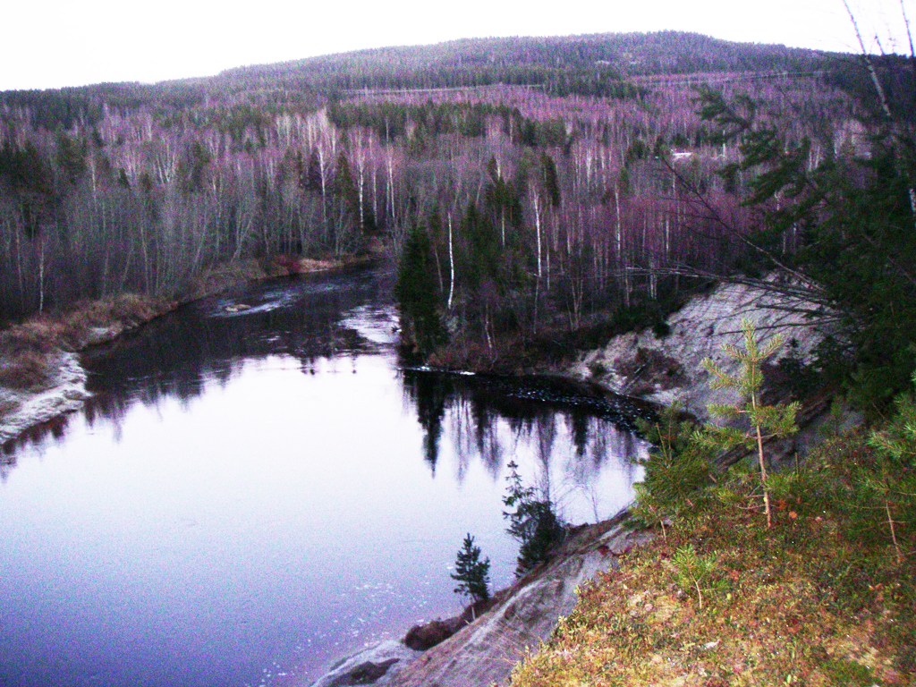 An aerial photo of a river winding through a forest. There is some snow on one of the riverbanks.